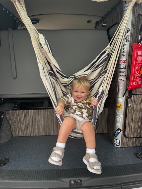 Young child smiling in a hammock swing inside the campervan